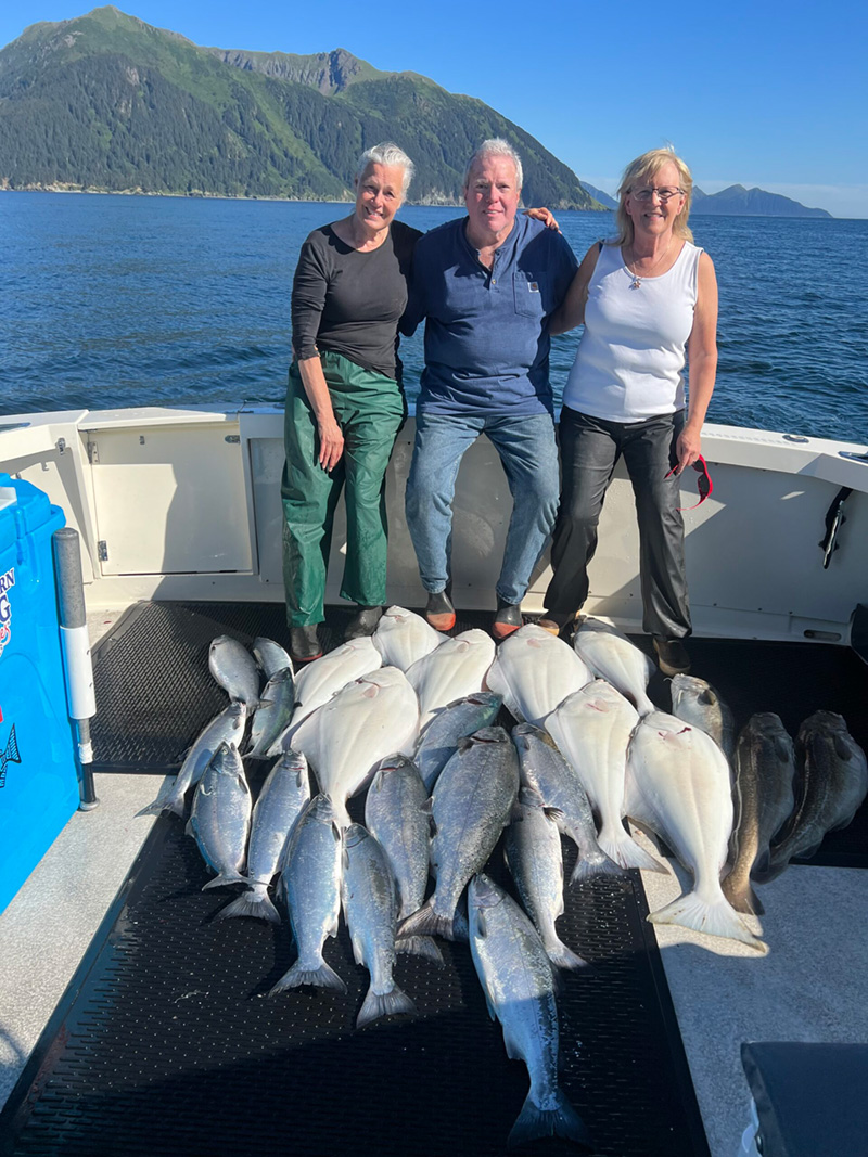 Three fishermen sit behind their catch of fish on a sunny day.