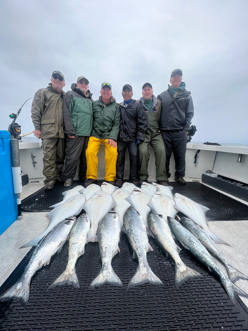 Six fishermen stand behind their catch happily.