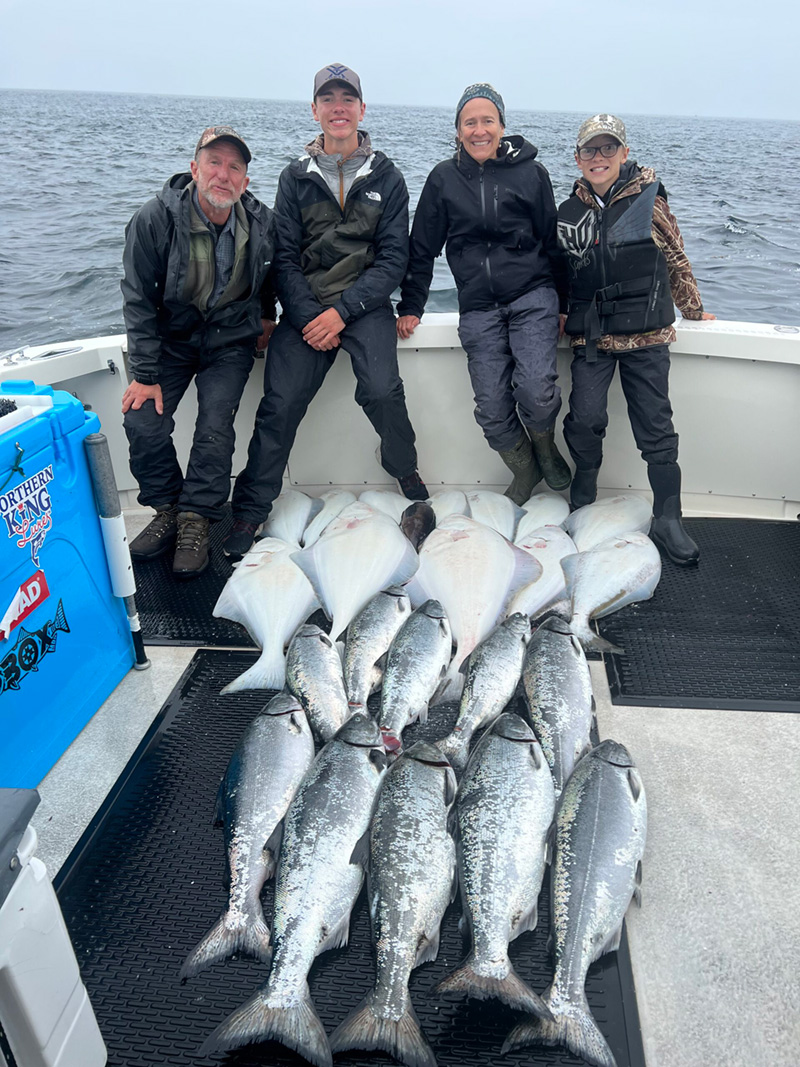 Two adults and two kids stand behind their catch happily.