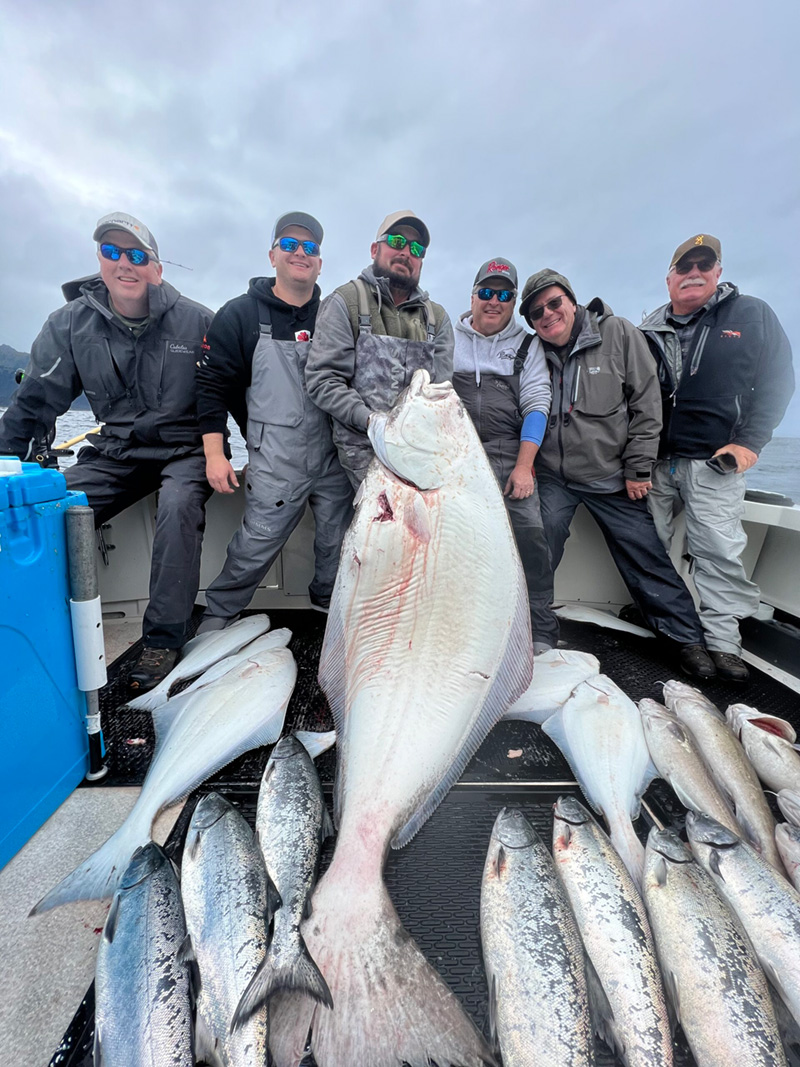 Six fishermen sit behind their catch while holding up a large sturgeon.